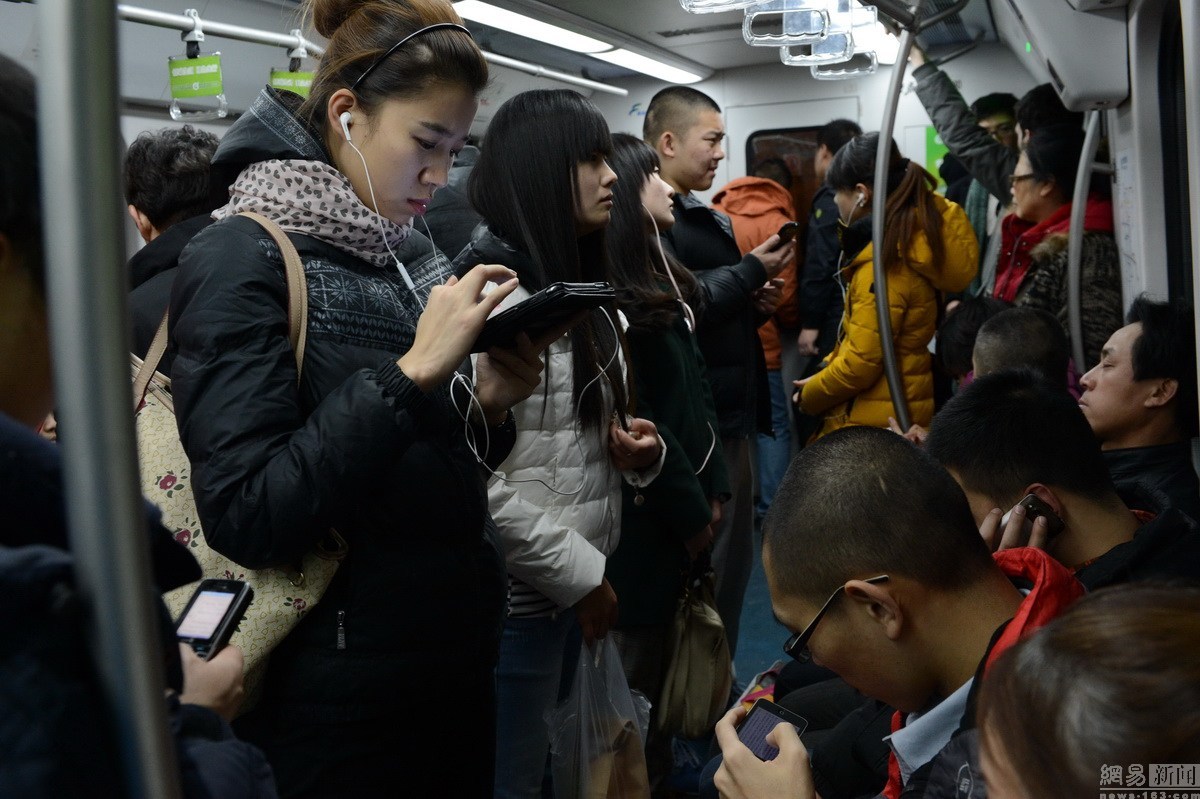 搭乘地铁二号线的乘客们看着各自的手机消磨时间.